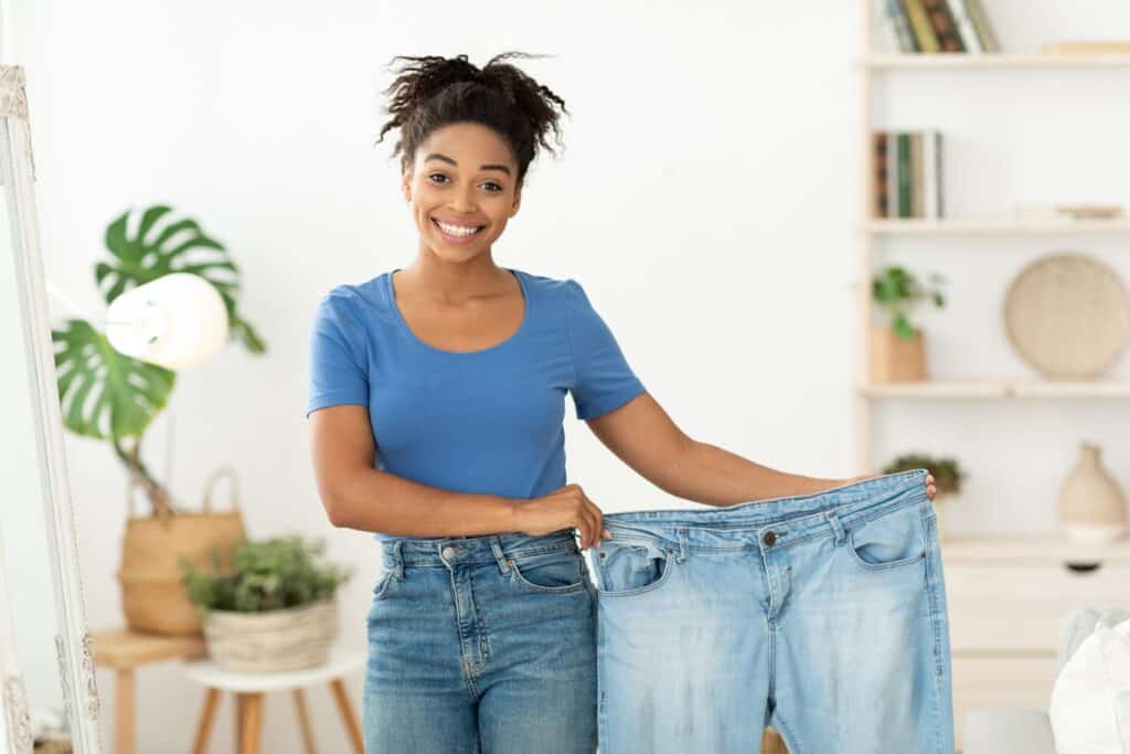 woman holding up her old jeans to show her weight loss transformation